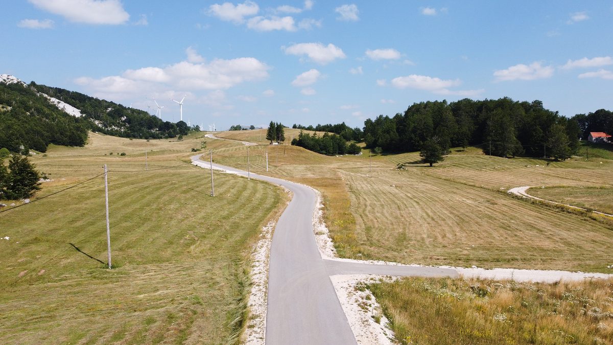 The asphalt road to the estate, with the Krnovo wind farm beyond.
